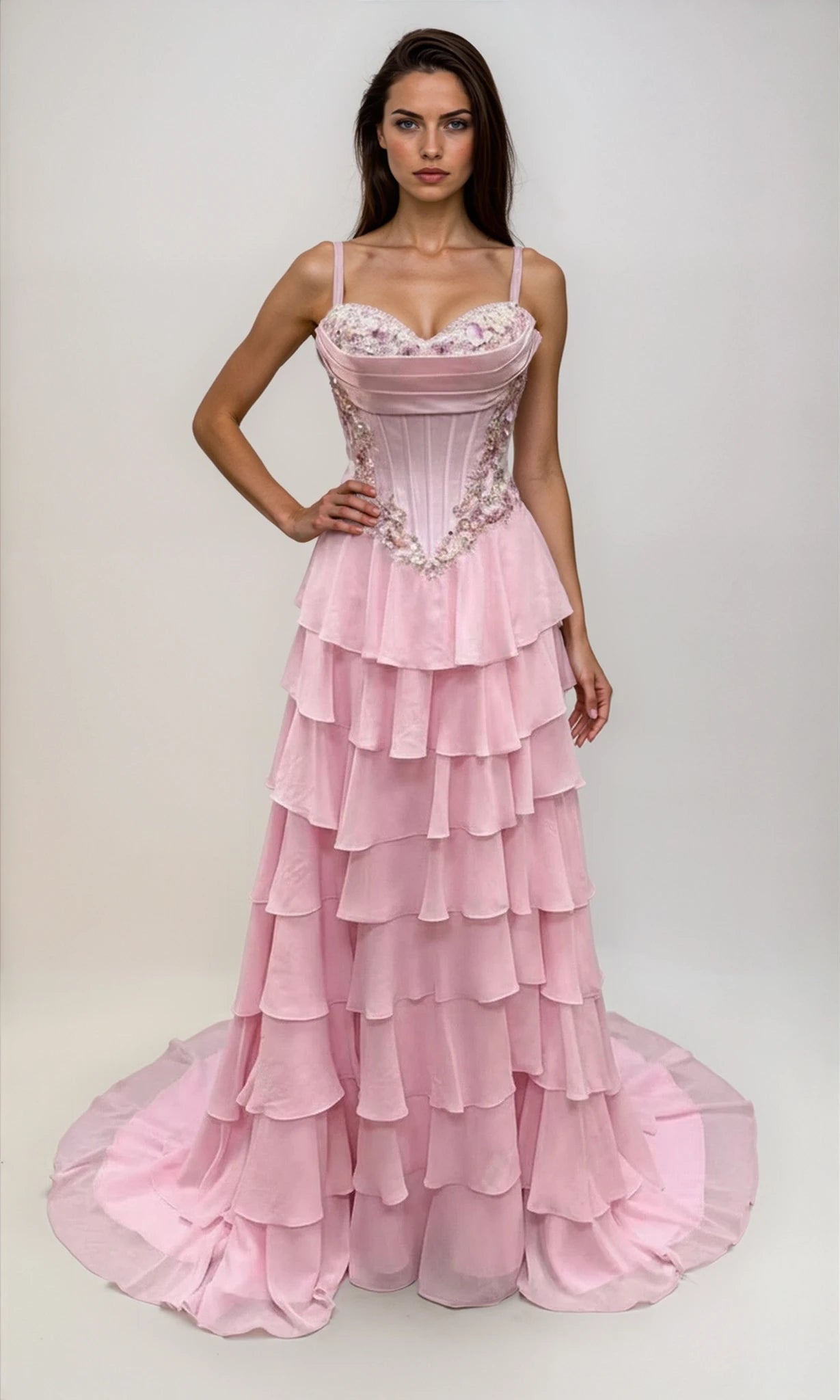 Woman in a pink Dave & Johnny 12966 long tiered A-line prom dress with a fitted, bead-trimmed corset bodice and spaghetti straps, standing against a plain light background.